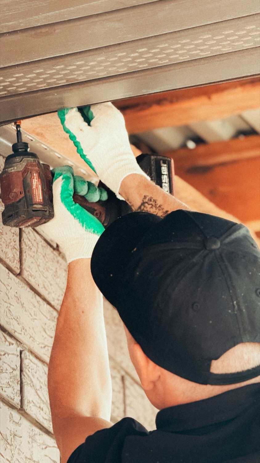 A handyman fastening trim under the eaves of a house with a cordless drill