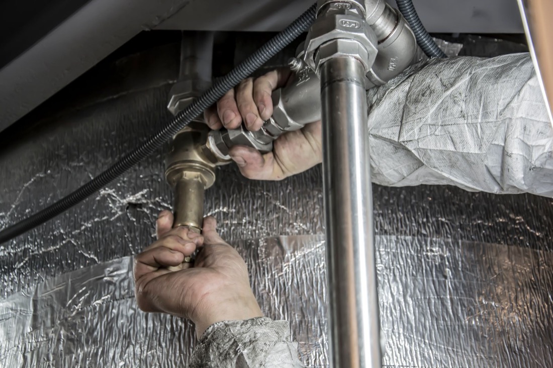 Hands tightening a fitting on copper and steel plumbing pipes